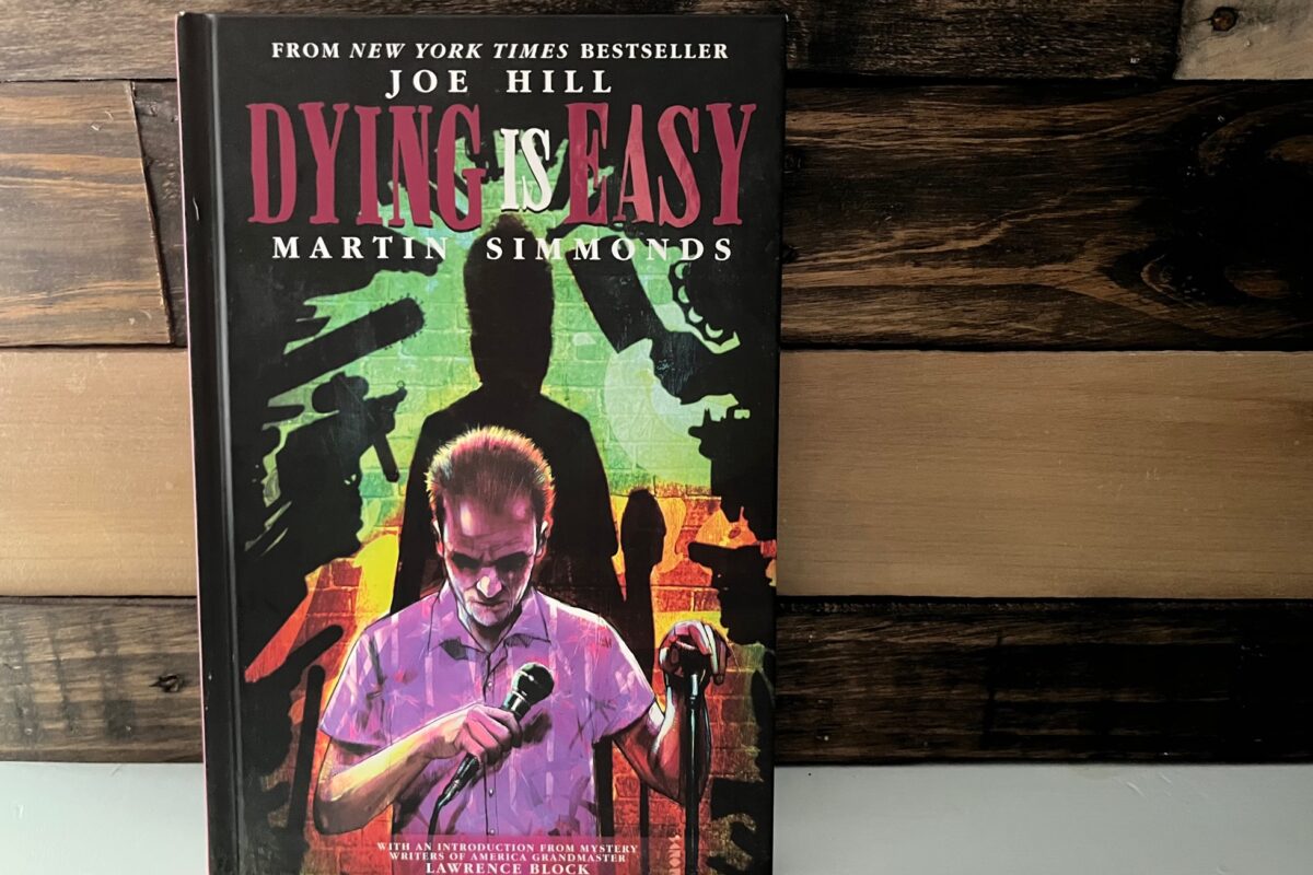 Dying is Easy by Joe Hill & Martin Simmonds graphic novel photo of man on a stage with lots of weapons in the shadows behind him