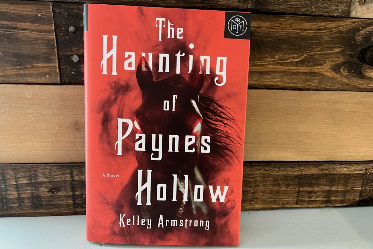 Book photo of The Haunting of Paynes Hollow by Kelley Armstrong featuring a dark horse with fiery red eyes